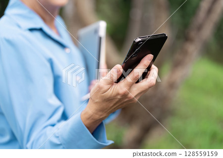 Business Professional Using Smartphone and Tablet Outdoors in a Natural Setting Business Professional Using Smartphone and Tablet Outdoors in a Natural Setting 128559159