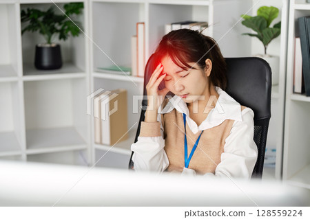 Young Office Worker Experiencing Headache Due to Office Syndrome in Modern Workspace with Shelves and Plants Young Office Worker Experiencing Headache Due to Office Syndrome in Modern Workspace with Shelves and Plants 128559224