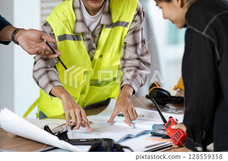 Engineer Construction Team collaboration on Project Plans in Modern Office Environment with Safety Gear and Equipment 128559358