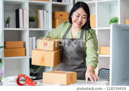 Small Business Owner Packing Boxes in Home Office for Online Delivery with Smiling Face and Organized Workspace Small Business Owner Packing Boxes in Home Office for Online Delivery with Smiling Face and Organized Workspace 128559439