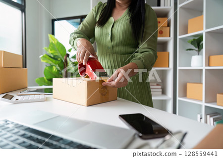 Small Business Owner Packing Orders in a Modern Home Office with Natural Light and Greenery 128559441