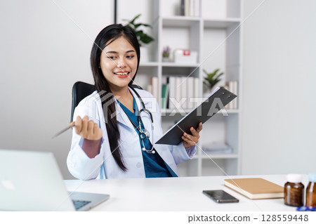 Young Female Doctor in White Coat Holding Clipboard and Pen in Modern Medical Office Young Female Doctor in White Coat Holding Clipboard and Pen in Modern Medical Office 128559448