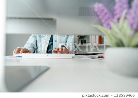 Woman Typing on Keyboard in Modern Office with Purple Flowers and Bookshelf in Background 128559466