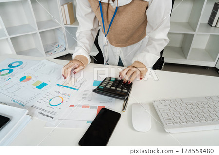 Businesswoman Analyzing Financial Reports with Calculator at Modern Office Desk Businesswoman Analyzing Financial Reports with Calculator at Modern Office Desk 128559480