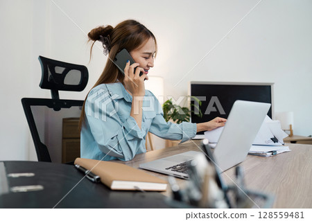 Professional Businesswoman Working at Desk with Laptop and Phone in Modern Office Setting Professional Businesswoman Working at Desk with Laptop and Phone in Modern Office Setting 128559481