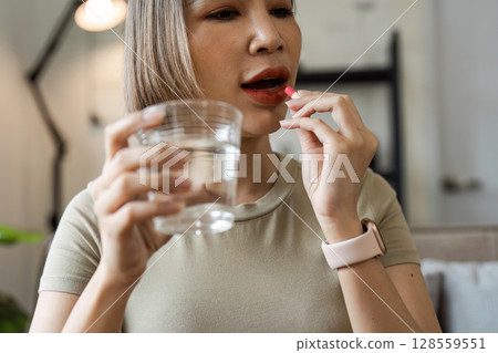 Woman Taking Medication with Water in a Modern Home Setting for Healthcare and Wellness Concept Woman Taking Medication with Water in a Modern Home Setting for Healthcare and Wellness Concept 128559551