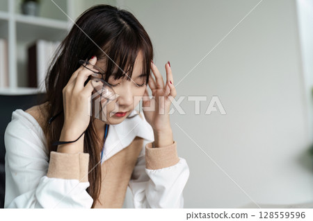 Stressed Office Worker Experiencing Headache Due to Office Syndrome in Modern Workplace Environment 128559596