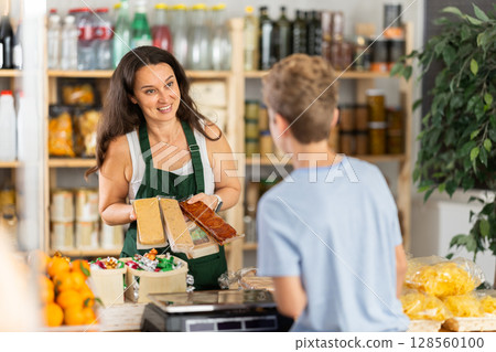 Female seller offers nougat to boy buyer 128560100