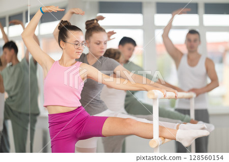 Ballet pose grand batman - girls and boys at a choreography lesson are learning ballet movements in studio Ballet pose grand batman - girls and boys at a choreography lesson are learning ballet movements in studio 128560154