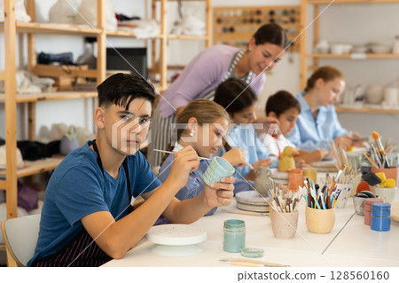 Teenage boy painting ceramic cupin pottery workshop 128560160