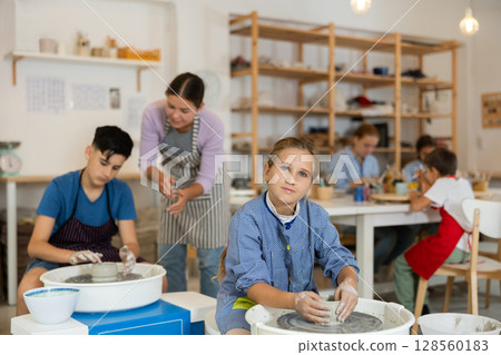 Girl working at a potter's wheel with clay Girl working at a potter's wheel with clay 128560183