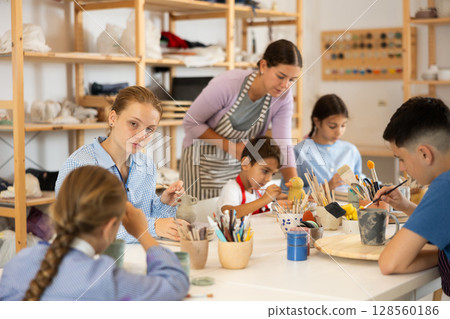 Children painting ceramics with a teacher 128560186