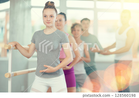 Teenagers doing ballet at group training session in the studio performs demi plie near the ballet barre, standing in ballet stance 128560198