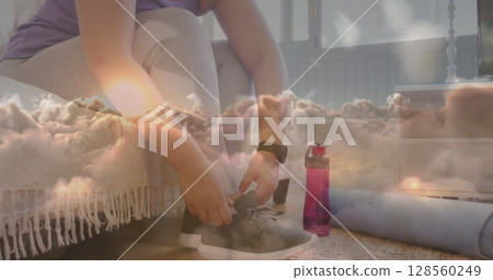 Image of sunset and clouds over woman tying shoe laces, exercising at home Image of sunset and clouds over woman tying shoe laces, exercising at home 128560249