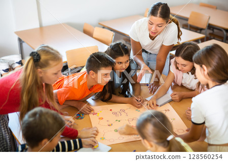 Schoolkids playing board game with teacher in classroom 128560254