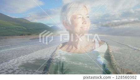 Image of glowing light over smiling senior woman by seaside Image of glowing light over smiling senior woman by seaside 128560302