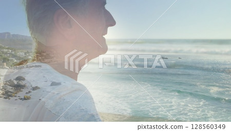 Image of glowing light over portrait of happy senior man by seaside Image of glowing light over portrait of happy senior man by seaside 128560349