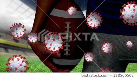 Covid-19 cells floating against mid section of male rugby player holding ball against sports stadium Covid-19 cells floating against mid section of male rugby player holding ball against sports stadium 128560502