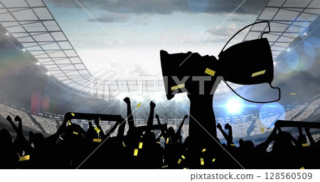Golden confetti falling over silhouette of fans cheering and sports stadium in background 128560509