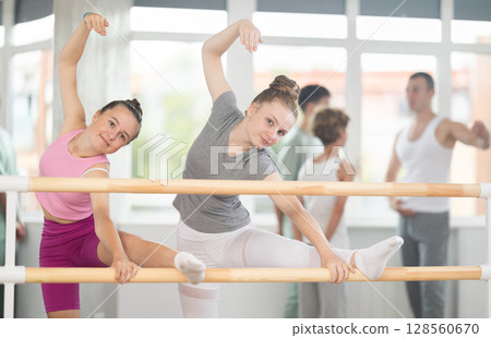 Teen ballet students prepare for classes, near ballet bare stretch legs under man teacher guidance 128560670