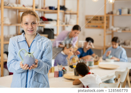 Girl holds a clay product against the background of students and a teacher Girl holds a clay product against the background of students and a teacher 128560770