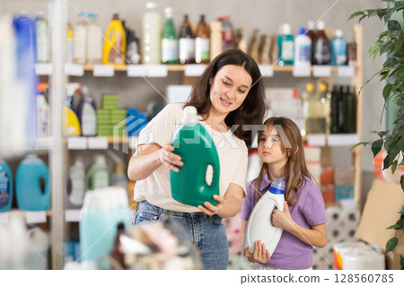 Woman and daughter buyer selects and carefully studies label, reads composition of liquid detergent 128560785
