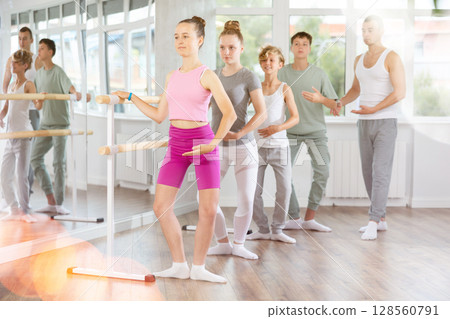 Male teacher conducts class with teens in ballet studio, observes doing plie exercise. Male teacher conducts class with teens in ballet studio, observes doing plie exercise. 128560791