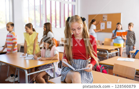 Portrait of clever schoolgirl with copybook in classroom 128560879