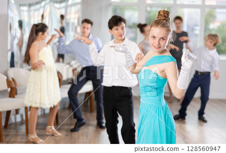Teen girl in elegant evening dress dances incendiary twist with boy partner during choreography lesson Teen girl in elegant evening dress dances incendiary twist with boy partner during choreography lesson 128560947
