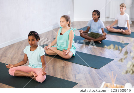In sport studio with group of friends, African girl perform lotus pose, with load on lateral muscles 128560949