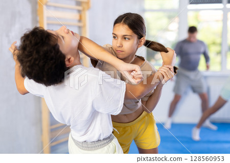 Group of children in sportswear exercising self protection techniques in pair during class at gym Group of children in sportswear exercising self protection techniques in pair during class at gym 128560953