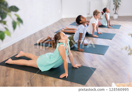 Children practicing yoga positions during group training in fitness center, performing stretching asana Urdhva Shvanasana 128560995