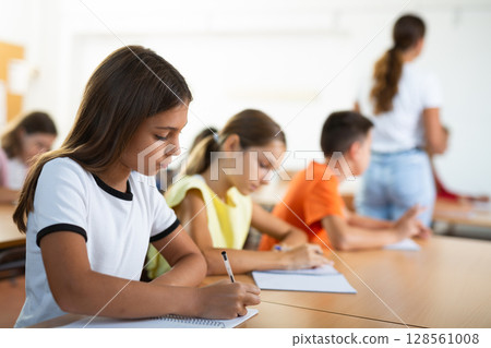 Assiduous focused tween girl sitting with pen and notebook at lesson Assiduous focused tween girl sitting with pen and notebook at lesson 128561008