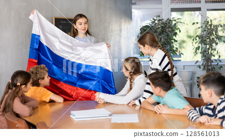 Pupils having lesson of geography. Female teacher discussing with children about national flag of Russia 128561013