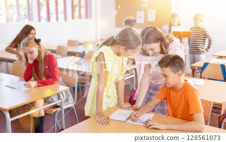 Two schoolgirls helping classmate to complete written assignment 128561073