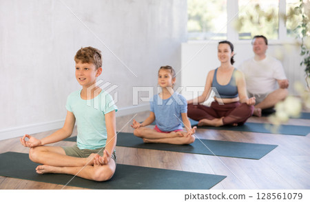 Calm preteen boy practicing lotus pose of yoga with his family Calm preteen boy practicing lotus pose of yoga with his family 128561079