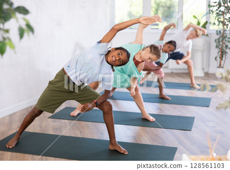 Children standing in Parivrtta Trikonasana or Revolved Triangle Pose on mats during group yoga training in fitness center Children standing in Parivrtta Trikonasana or Revolved Triangle Pose on mats during group yoga training in fitness center 128561103