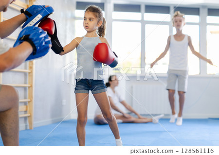 Tween girl in boxing gloves practicing punches on focus mitts in hands of father 128561116