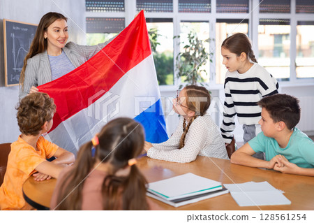 Teacher holds the flag of Netherlands in her hands and tells students about this country 128561254