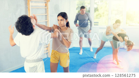 Girls and boys practicing in pair self defence movements with female trainer supervision 128561275