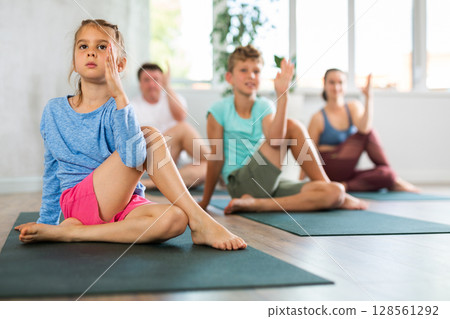 Pleasant little girl practicing half lord of the fishes pose of yoga with her family 128561292