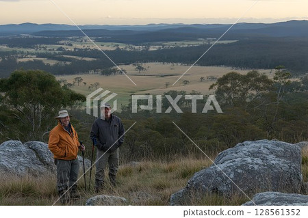 Hikers pause on grassy hilltop overlooking valley, mountains in 128561352