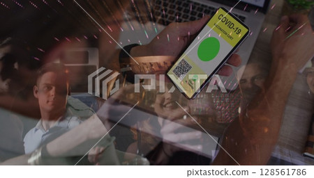 Image of man holding smartphone with covid 19 vaccination passport over people having fun 128561786