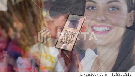 Woman holding a smartphone with qr code on screen against caucasian woman drinking a smoothie 128561812