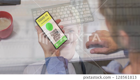 Man holding a smartphone with qr code on screen against female baker smiling at cake shop 128561813