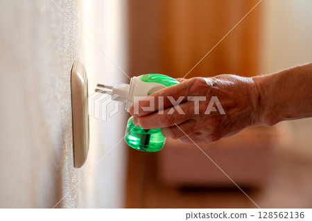 Woman hand plugs mosquito repellent into the socket before going to bed. Insect repellent diffuser. 128562136