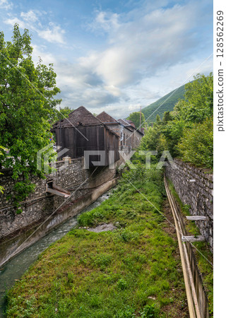 Old traditional building with distinctive wooden facade and water channel in Sheki, Azerbaijan, against a mountain backdrop Old traditional building with distinctive wooden facade and water channel in Sheki, Azerbaijan, against a mountain backdrop 128562269