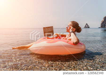 Woman, Laptop, Beach: Working remotely on a tropical beach while floating on an inflatable ring. 128562340