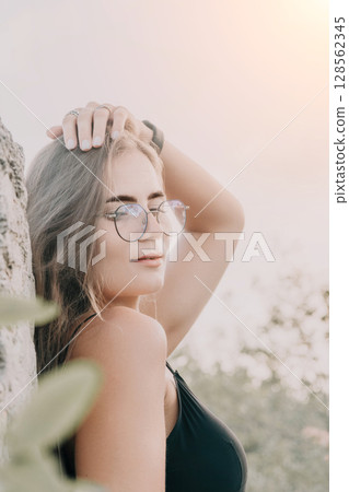 Woman Glasses Beach Portrait - Woman in glasses standing by a tree on the beach looking away from the camera. 128562345
