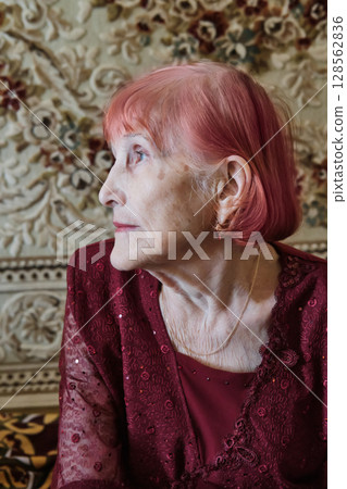 Elderly caucasian woman with pink hair in elegant red attire looking away Elderly caucasian woman with pink hair in elegant red attire looking away 128562836